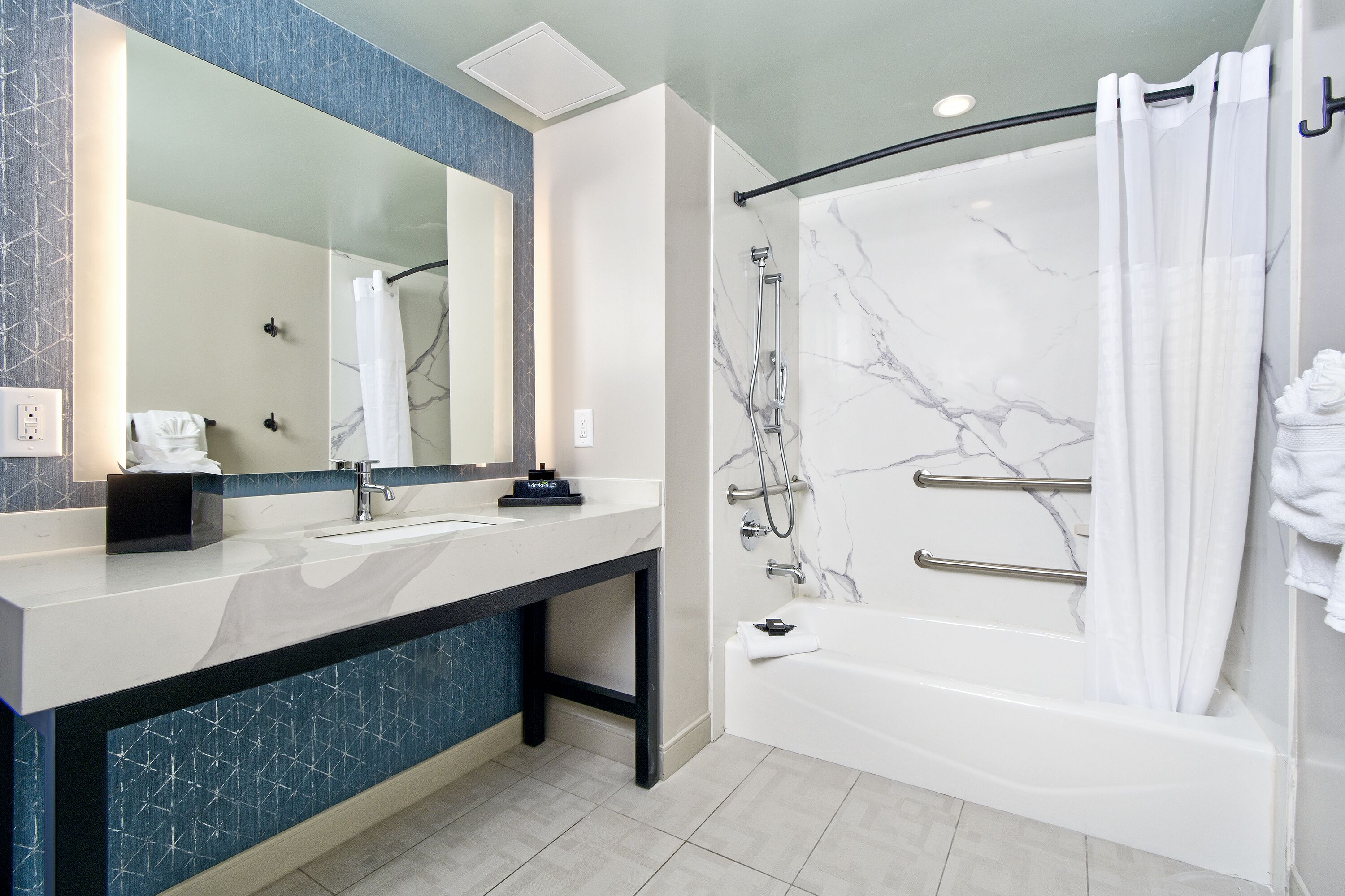 A modern bathroom with a marble shower, a large mirror, and a vanity with a sink and towel rack.