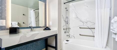 A modern bathroom with a marble shower, a large mirror, and a vanity with a sink and towel rack.