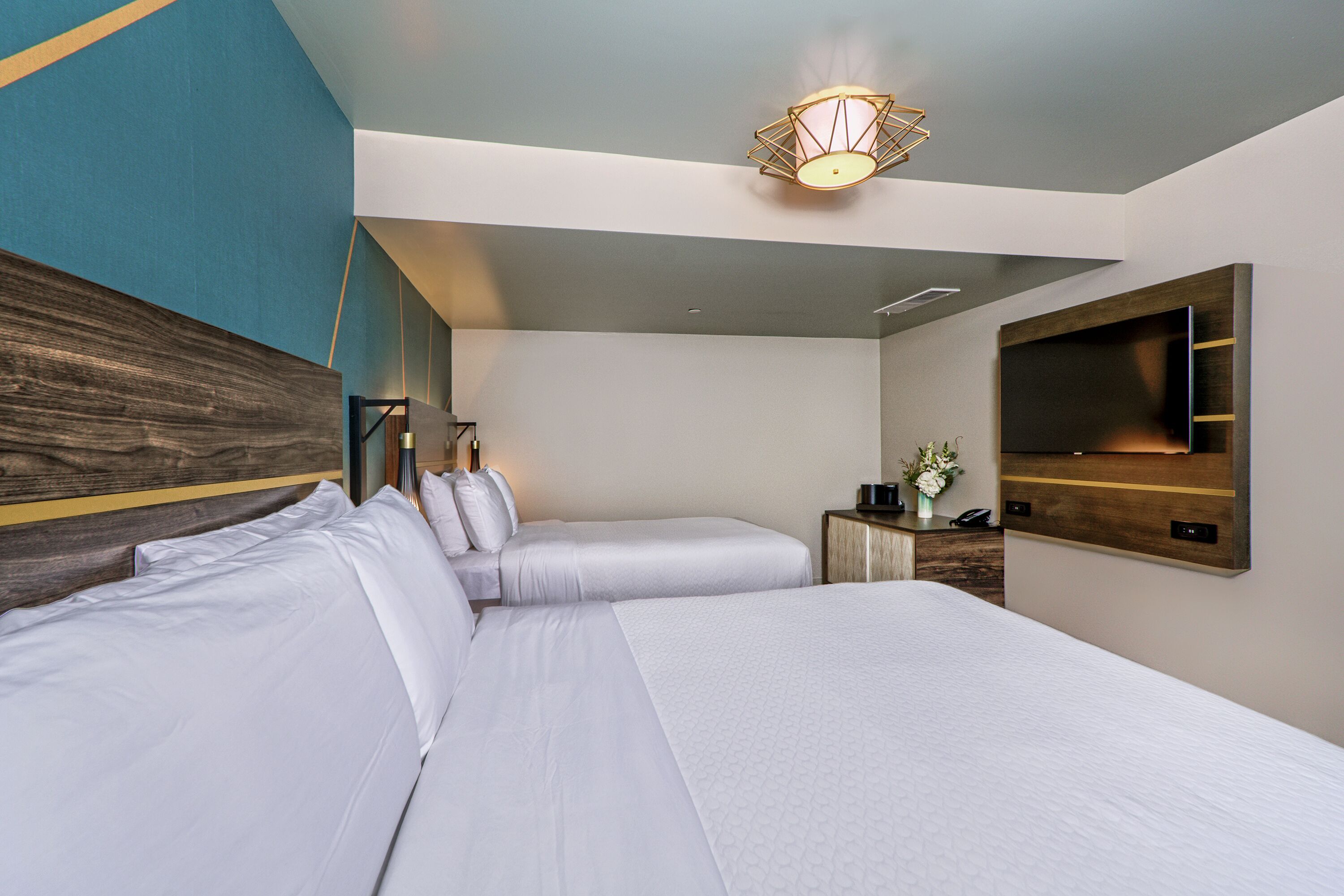 Una habitación de hotel moderna con una cama grande, una mesita de noche con lámpara, un televisor de pantalla plana en la pared y un panel decorativo.