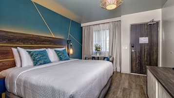 Una habitación de hotel moderna con una cama grande, cabecera de madera, escritorio y zona de comedor.