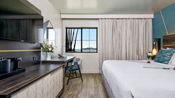 Habitación de hotel con cama, un escritorio con silla, televisor, ventana con cortinas y vista a la ciudad.