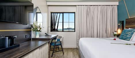 A hotel room with a bed, a desk with a chair, a TV, a window with curtains, and a view of the city.