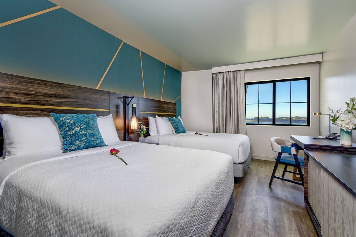 A hotel room with two beds, a desk, and a view of the city.
