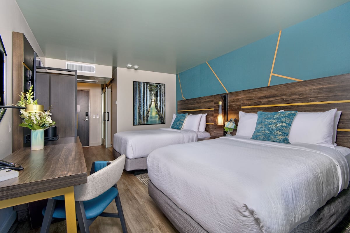A hotel room with two beds, a desk, and a chair.
