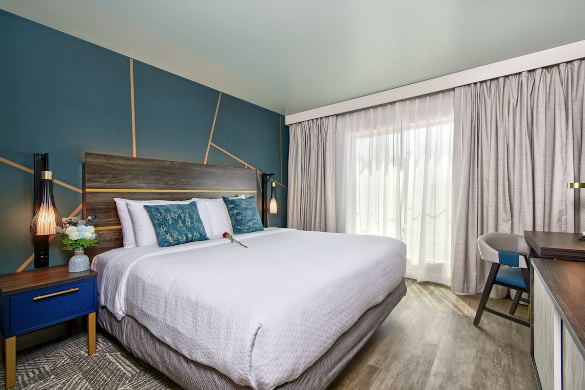 A modern hotel room with a large bed, a desk, and a chair.
