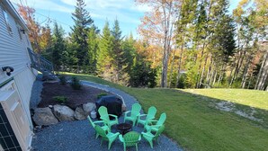 Un patio con una mesa de madera y cuatro sillas Adirondack verdes, rodeado de grava y un césped.