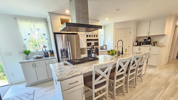 Una cocina moderna con una isla central, muebles blancos, electrodomésticos de acero inoxidable y un comedor con sillas blancas.