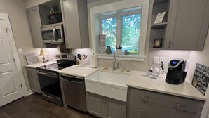 Una cocina moderna con gabinetes grises, horno empotrado, microondas, cafetera y ventana con vista a árboles.