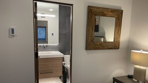 A modern bathroom with a wooden vanity, a mirror, and a bedside table with a lamp.