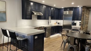 A modern kitchen with dark cabinetry, a central island, and a dining area with metal chairs.
