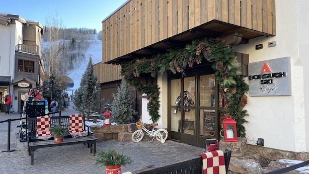 A wooden building with a sign for 'Gorsuch Ski Cafe'. There are Christmas decorations, a bicycle, and a bench outside.