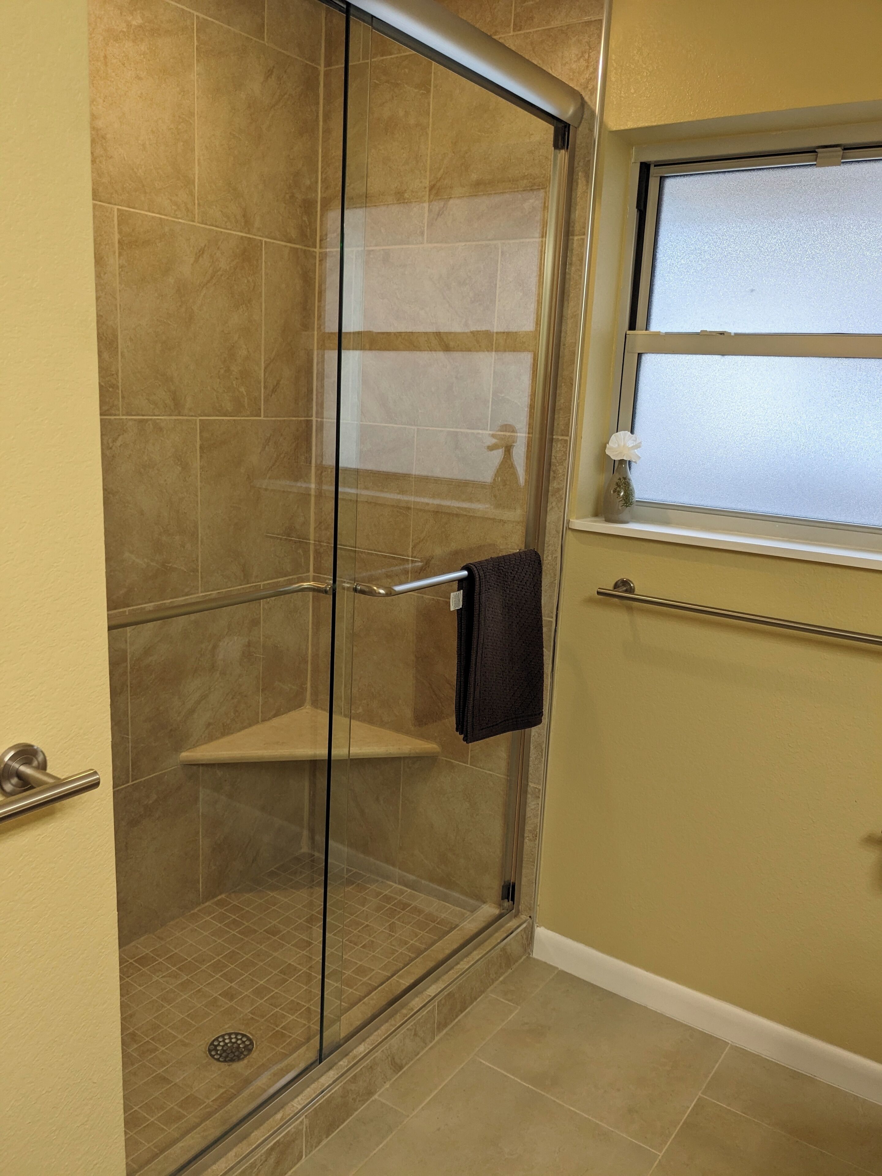 Une douche fermée par des parois de verre, avec un porte-serviettes et une fenêtre au-dessus.