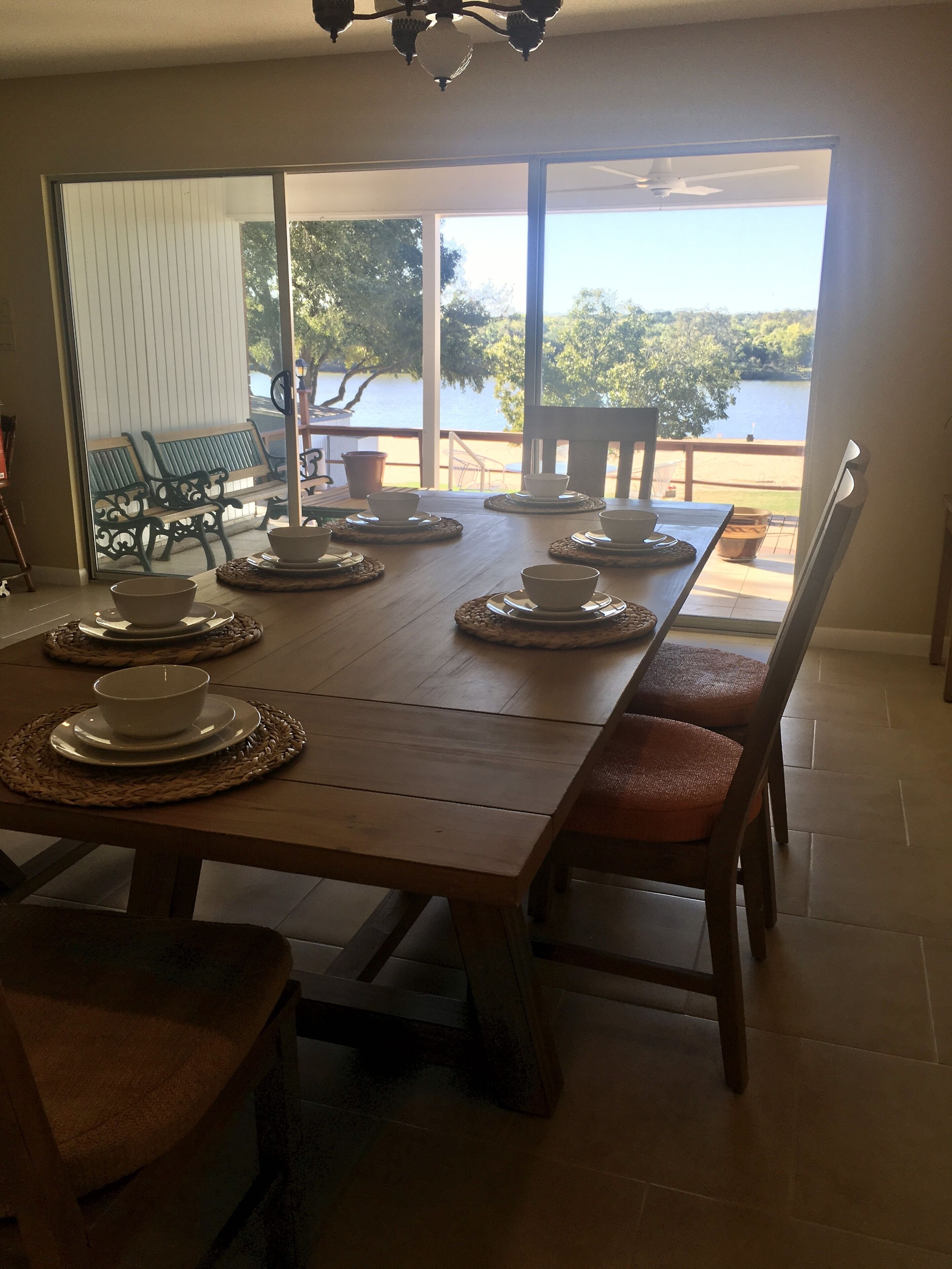 A dining area with a large table set for four, chairs, and a view of a lake through large windows.