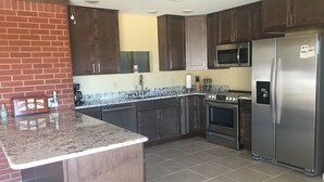 Una cocina moderna con armarios de madera oscura, electrodomésticos de acero inoxidable, encimera de granito y suelo de baldosas.