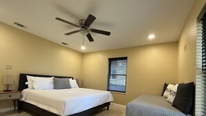 Un dormitorio con cama, mesita de noche, silla, ventilador de techo y ventana con persianas.
