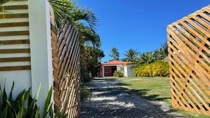 A gravel pathway leading to a building with a red roof, surrounded by lush greenery and palm trees. - La Casita de Cabrera by Cabrera Lodge (Nagua)