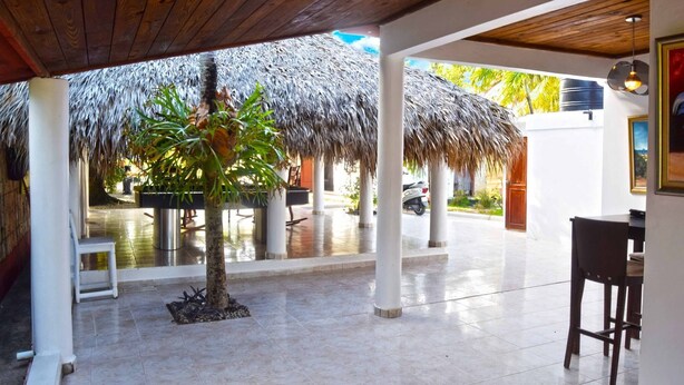 A covered outdoor area with a thatched roof, white pillars, and a tiled floor. - La Casita de Cabrera by Cabrera Lodge (Nagua)
