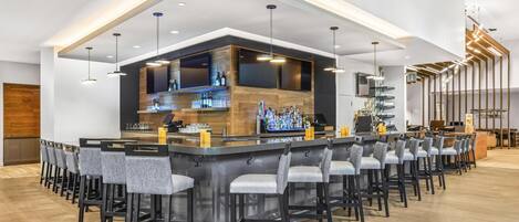 Een moderne bar met een lange toonbank, diverse barkrukken en een ruim assortiment flessen en glazen.