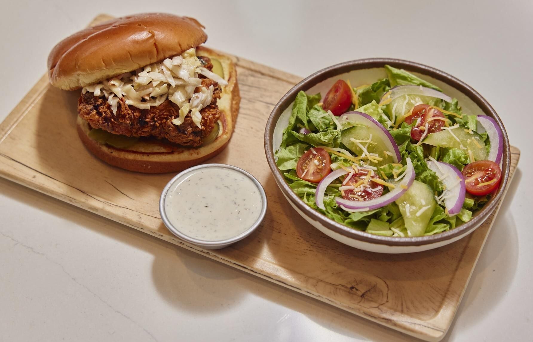 A meal consisting of a burger with coleslaw and a side salad with tomatoes, onions, and shredded cheese.