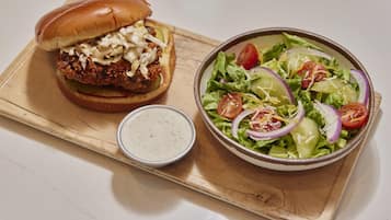 A meal consisting of a burger with coleslaw and a side salad with tomatoes, onions, and shredded cheese.
