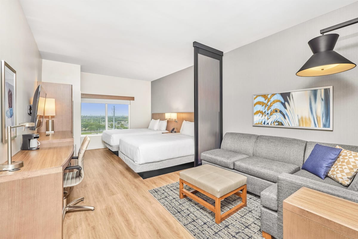 Ein modernes Hotelzimmer mit Bett, Sofa, Schreibtisch und einem großen Fenster mit Blick auf die Stadt.