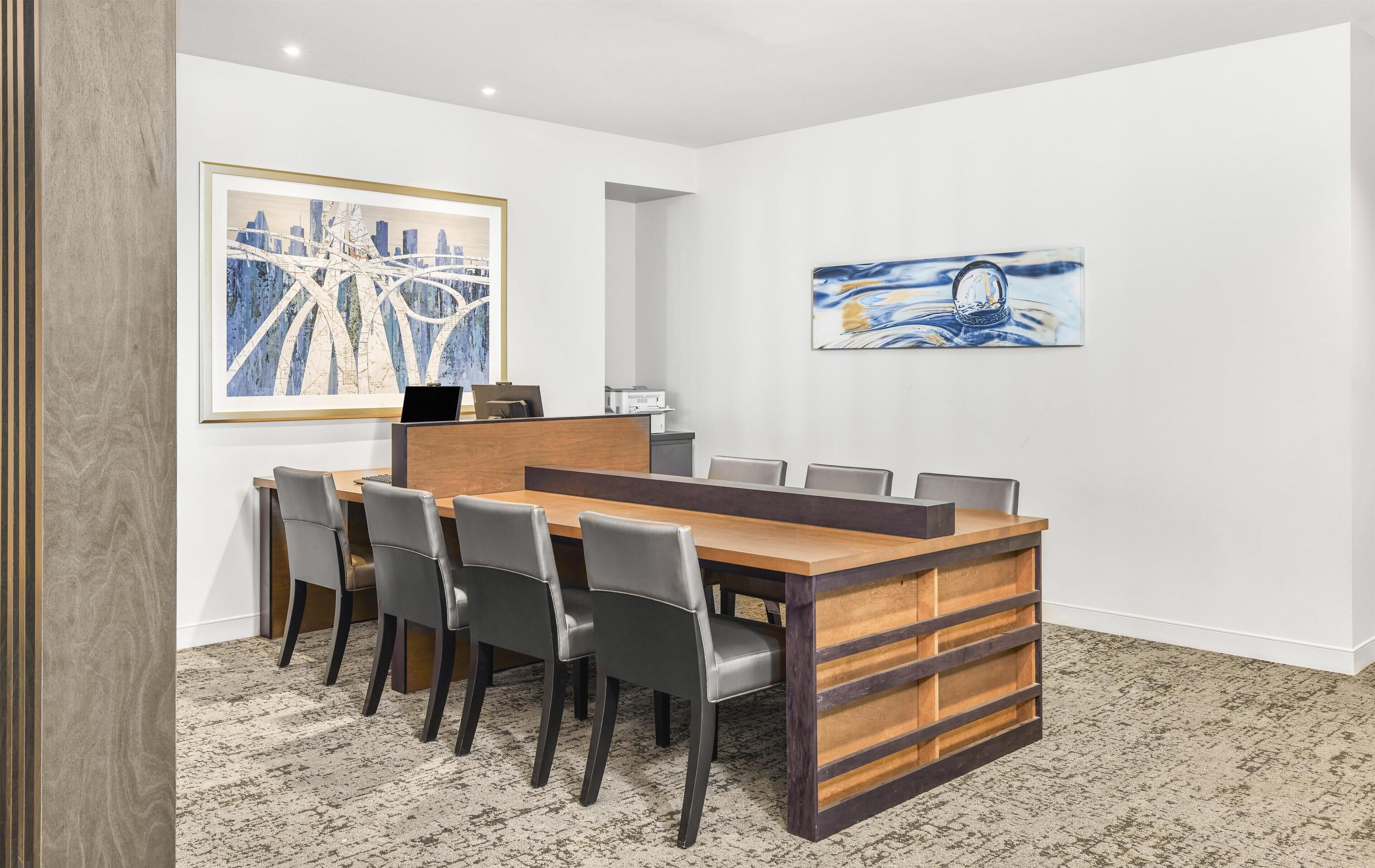 Une salle de conférence avec une longue table, six chaises et deux œuvres d’art encadrées accrochées aux murs.