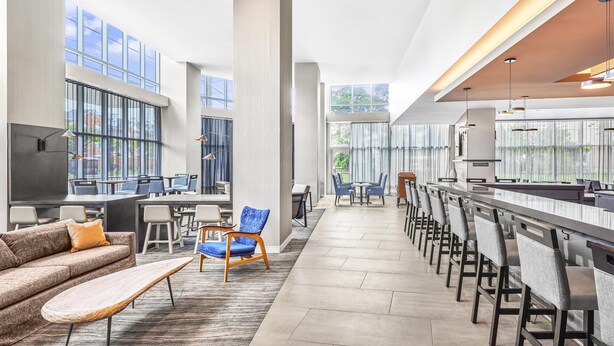 A spacious hotel lobby with high ceilings, large windows, a long bar area, and a seating area with a sofa and chairs. - Hyatt Place Houston Medical Center (Houston)