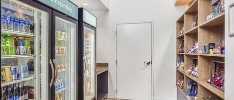 A corridor with beverage refrigerators stocked with drinks and snacks, and wooden shelves with packaged goods.