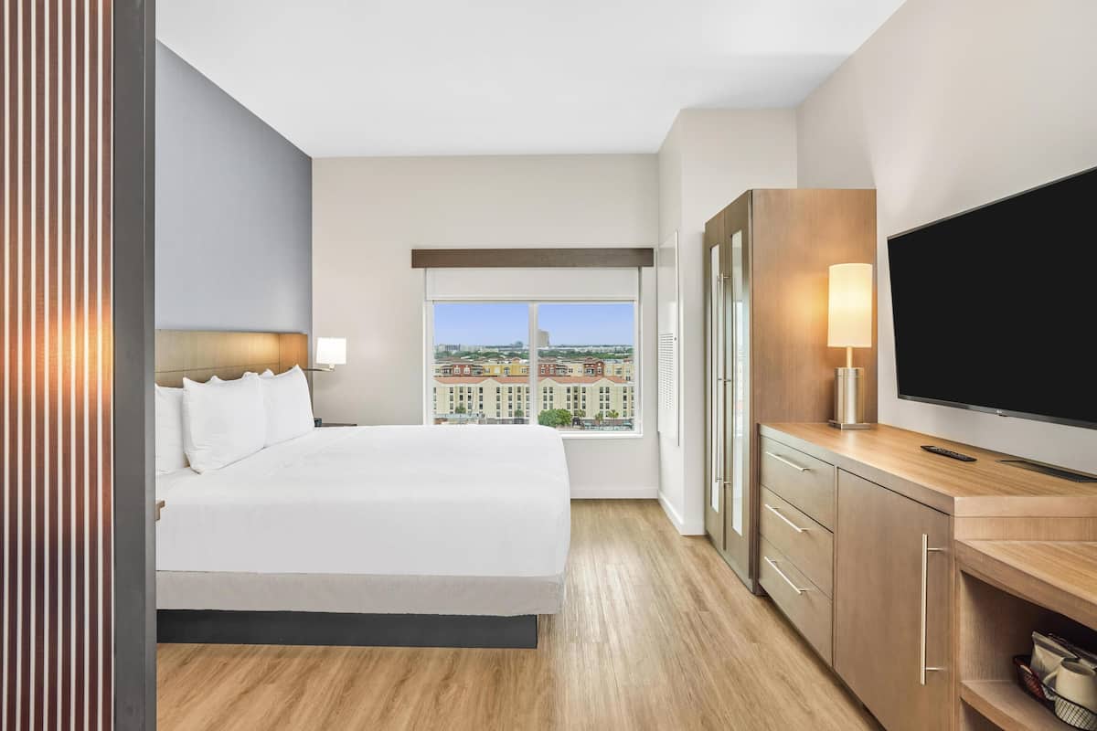 Ein Hotelzimmer mit einem großen Bett, einem Fernseher, einem Schreibtisch und einem Fenster mit Blick auf die Stadt.