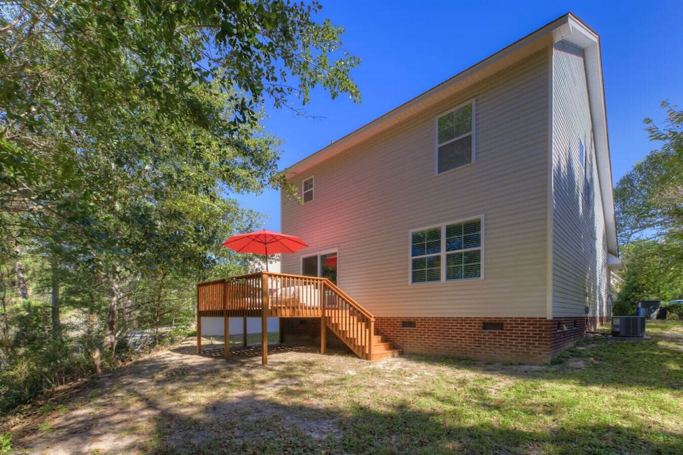 A two-story house with a wooden deck and a red umbrella.