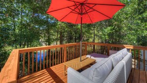 A wooden deck with a red umbrella, white wicker sofa, and a small table. - Pondside at Sweetoak | 4 BR | Mins to Ft Jackson (Columbia)