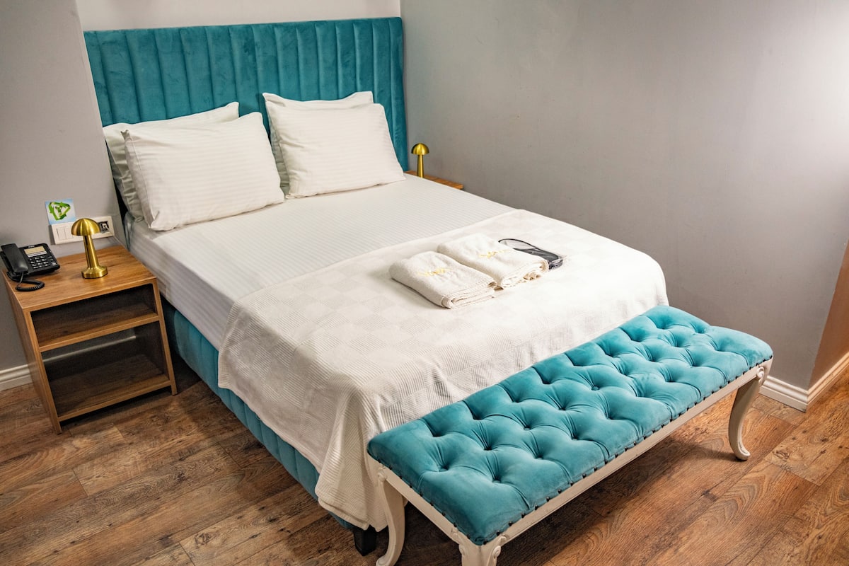 Una cama bien hecha con sábanas blancas, un cabecero verde azulado y un banco tapizado en azul.
