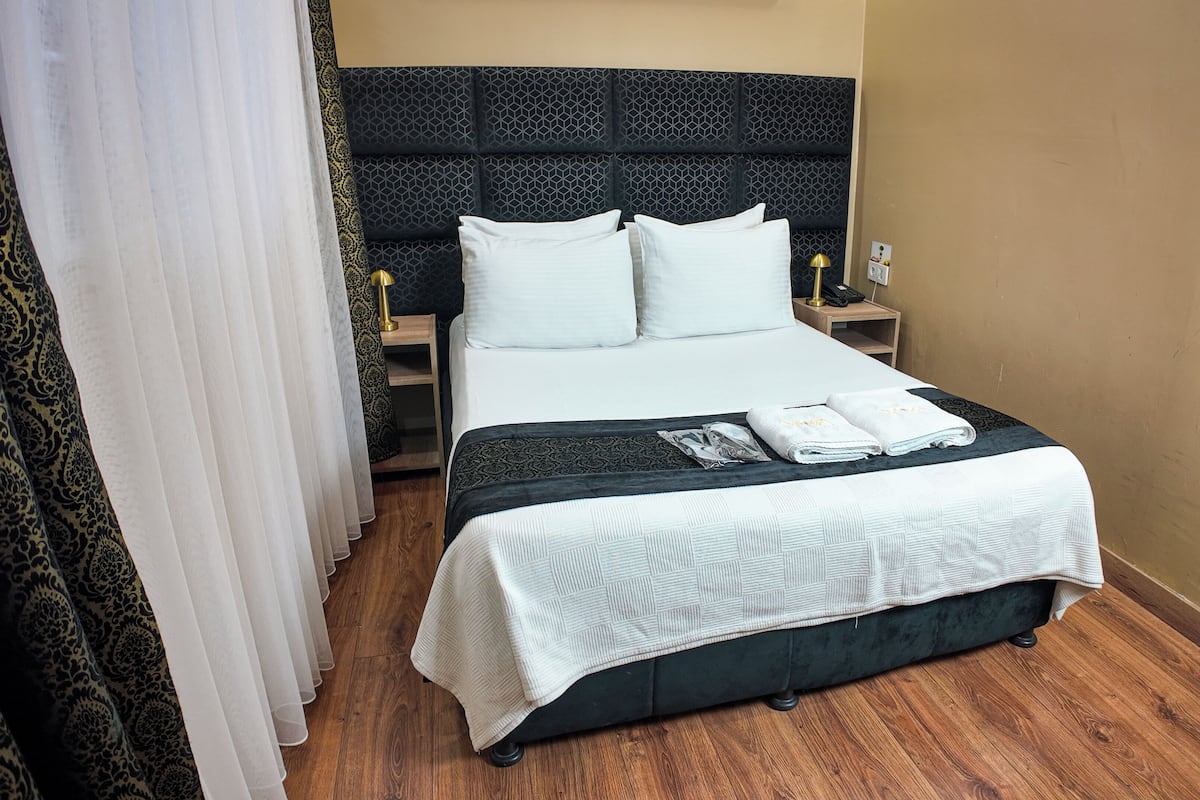 Una habitación de hotel con una cama grande, una mesita de noche con lámpara y otro mueble con un teléfono.