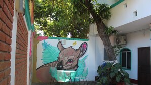 A courtyard with a mural of a deer, a table with chairs, and potted plants. - Hotel Gamito (Puerto Escondido)