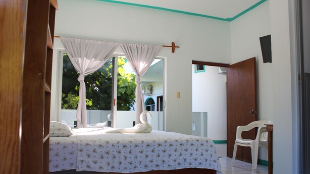 A bedroom with a bed, curtains, a chair, and a door. - Hotel Gamito (Puerto Escondido)