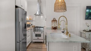 Een moderne keuken met witte kastjes, roestvrijstalen apparatuur, een gasfornuis en een groot eiland met een spoelbak en gouden kraanwerk.