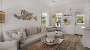 Een moderne woonkamer met een beige bank, een houten salontafel met decoratieve objecten, en een groot kunstwerk aan de muur.