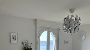 Ein modernes Wohnzimmer mit einer Couch, einem Esstisch mit Stühlen, einer Heizung und Meerblick durch ein großes Fenster.