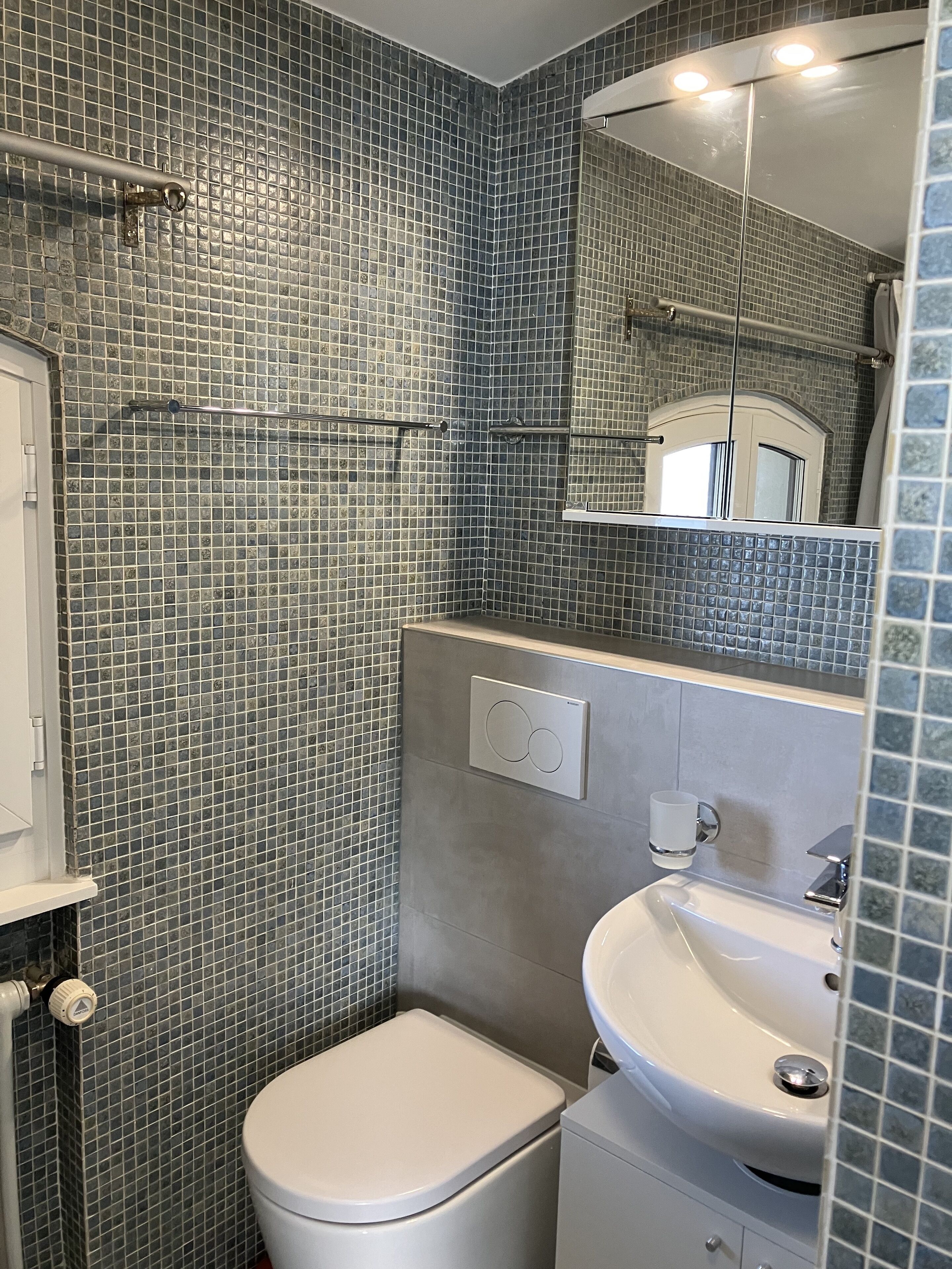 Ein Badezimmer mit gefliesten Wänden, einer Toilette, einem Waschbecken und einem Spiegel.