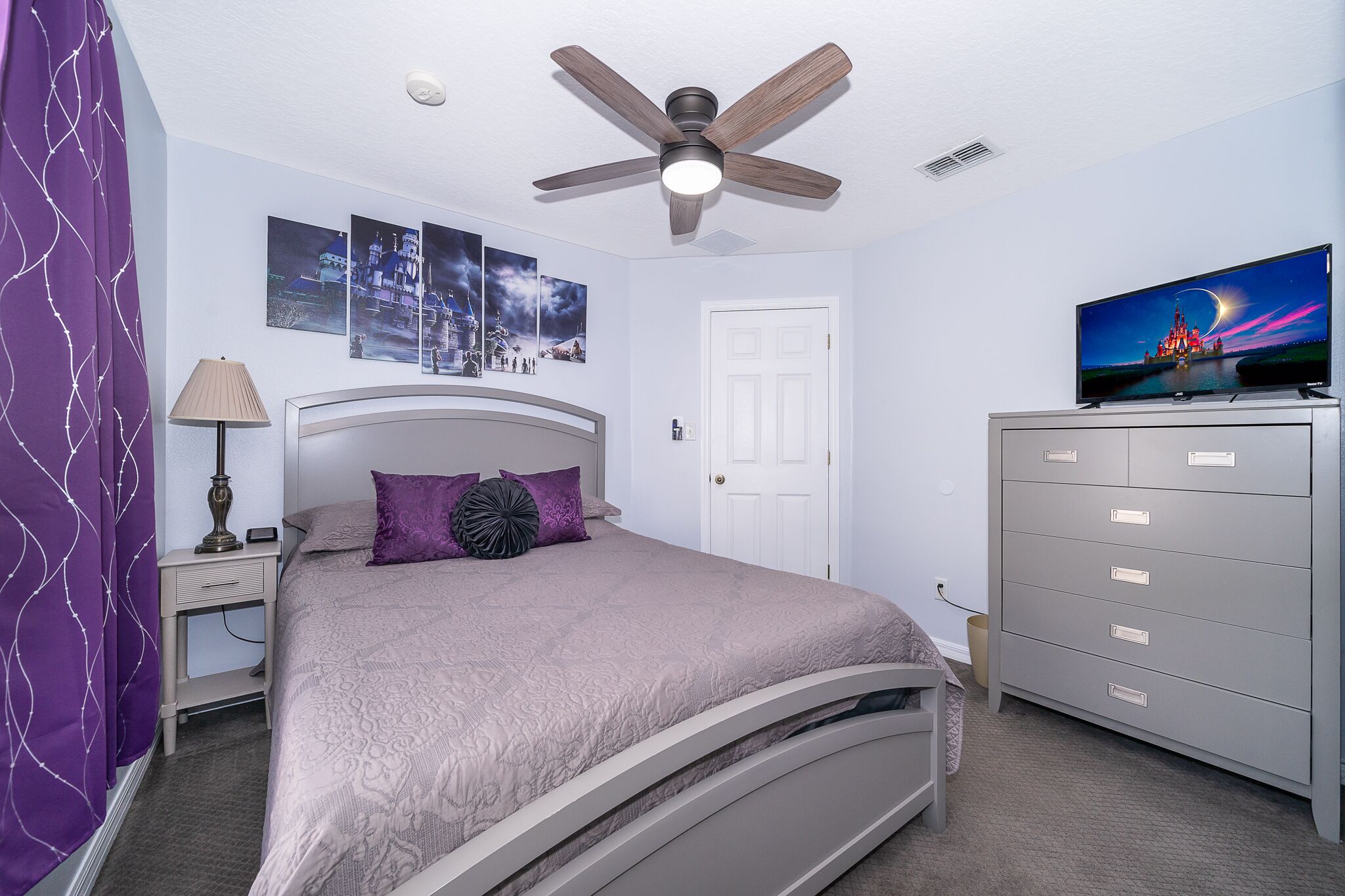 Een slaapkamer met een bed, een plafondventilator, een televisie, een dressoir en een deur.