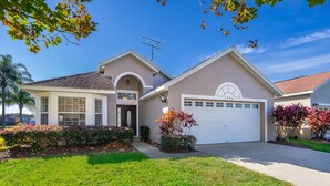 A two-story house with a garage, a front yard with a lawn and shrubs, and a clear blue sky. - Summer Breeze (Kissimmee)