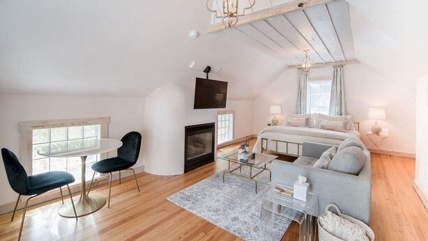 A modern loft bedroom with a large bed, a fireplace, a TV, and a dining area with chairs and a table.