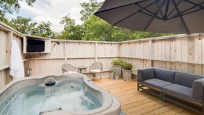A wooden deck with a hot tub, outdoor furniture, and a large umbrella.