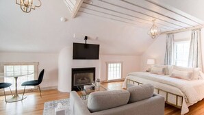 A modern bedroom with a bed, a sofa, a TV, and a fireplace.
