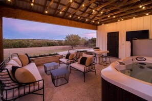An outdoor patio with a hot tub, seating area, and a view of the landscape. - Cedar Haus: Modern Guesthouse in Fredericksburg (Fredericksburg)
