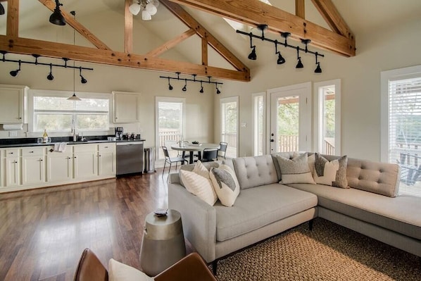 A spacious living area with a large sectional sofa, a kitchen with white cabinets, and a dining area with a table and chairs.