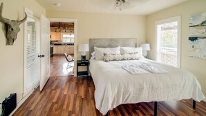 A bedroom with a large bed, bedside lamps, a ceiling fan, a kitchen in the background, and a bull skull decoration.