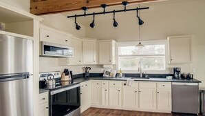 A modern kitchen with white cabinetry, stainless steel appliances, and a wooden ceiling.