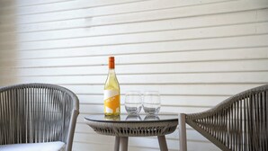 A wicker chair, a small round table, a bottle of wine, and two glasses on the table. - Cozy Modern Suite in Fredericksburg (Fredericksburg)