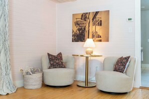 A room with two armchairs, a small table with a lamp, a wall-mounted picture, and a wicker basket.